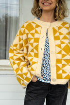 Person wearing a yellow and white geometric patterned cardigan outdoors.