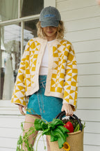 Woman wearing a yellow and white patterned jacket and blue denim skirt, holding a basket of groceries.