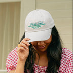 Woman wearing a white cap and red checkered dress holding a bouquet of greenery.
