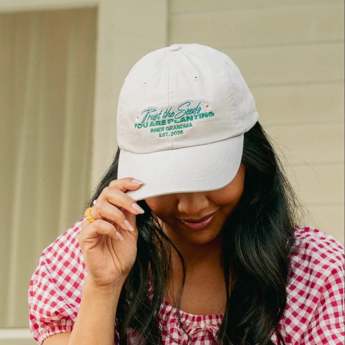 Woman wearing a white cap with text, smiling outdoors.