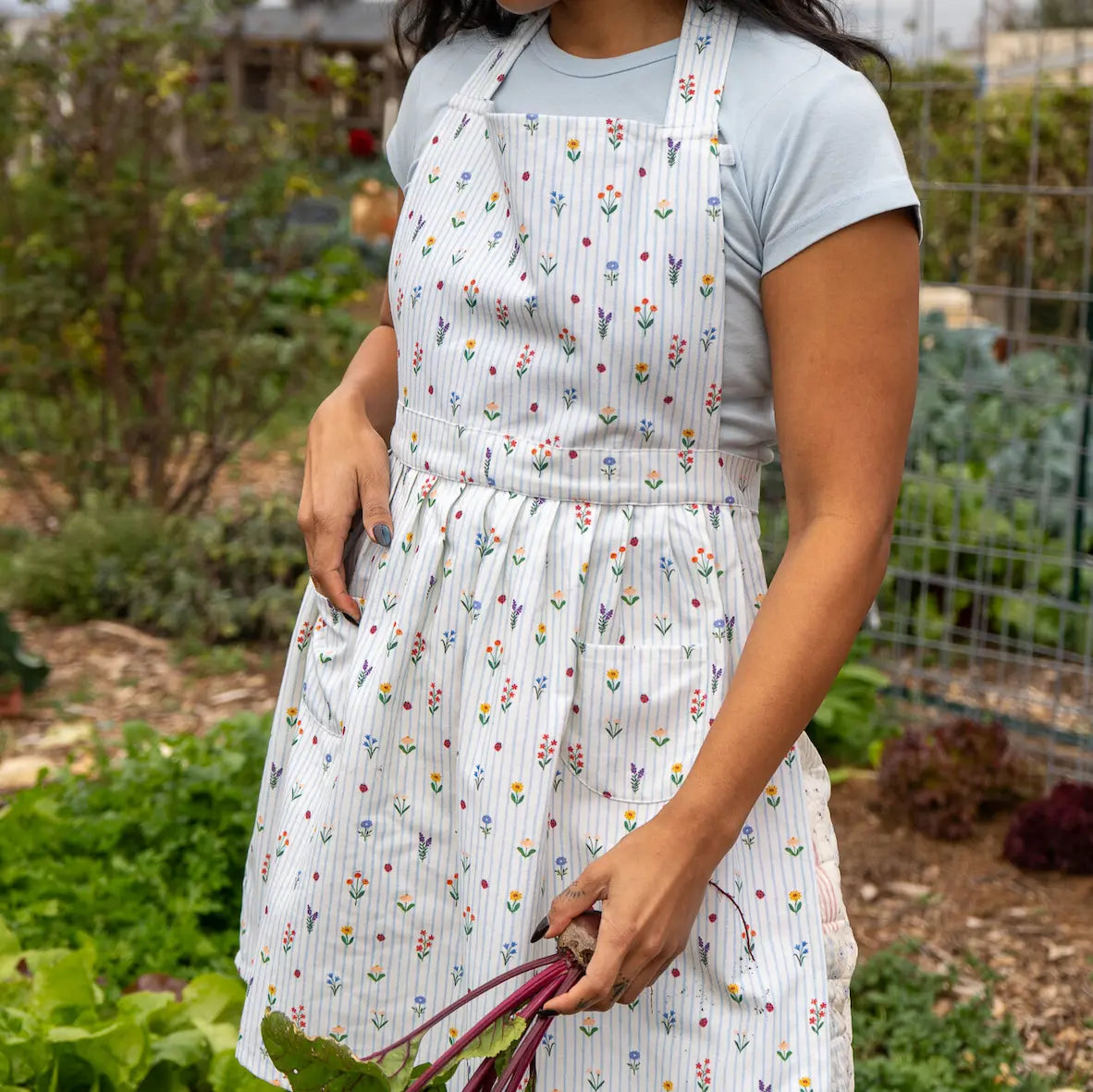 Women in garden with floral print apron with veggies in hand