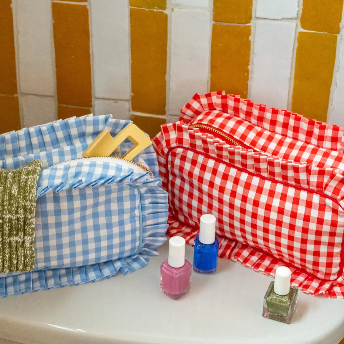 Nail polish bottles on a white surface with a checkered basket and red gingham towel in the background.