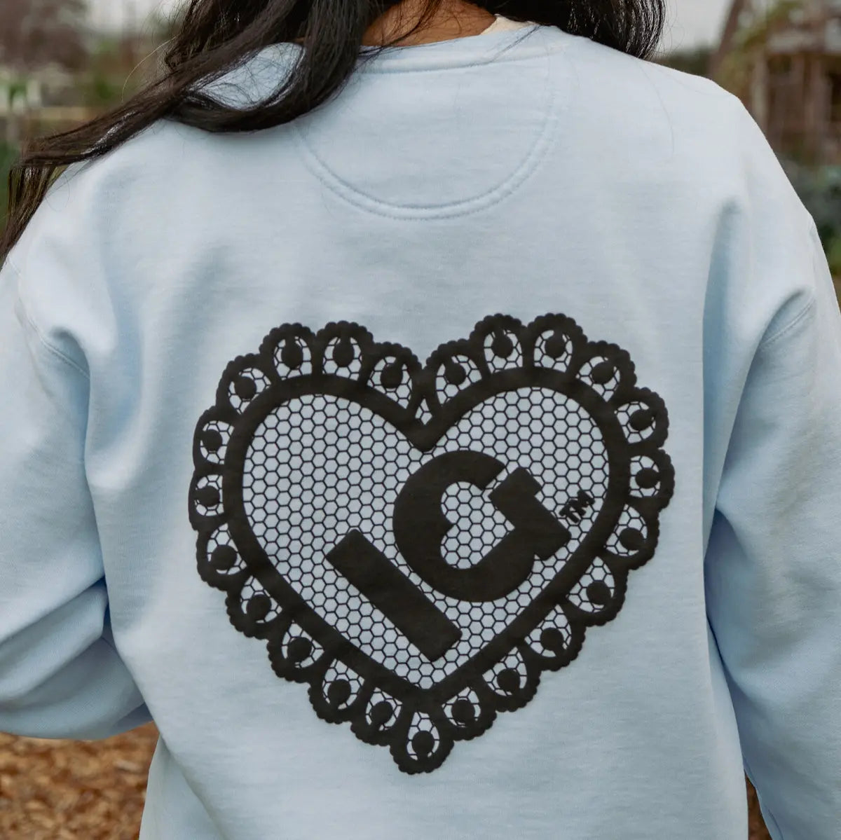 Light blue sweatshirt with a black heart design with "IG" on the back, worn by a person outdoors.