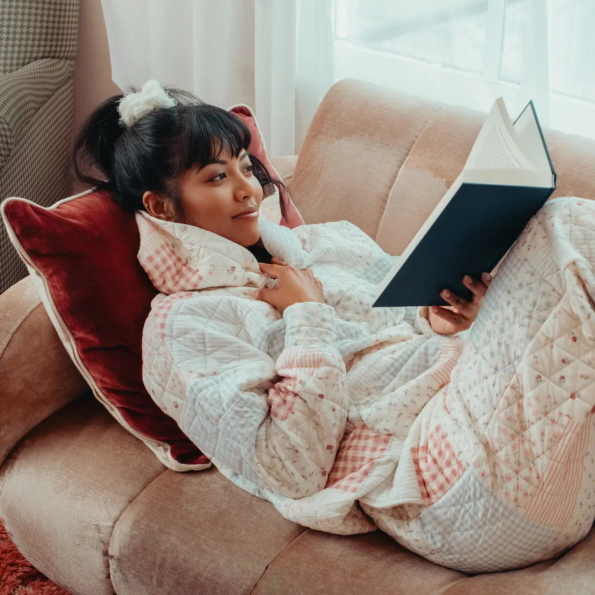 Person in cozy patchwork designed hoodie reading a book on a couch