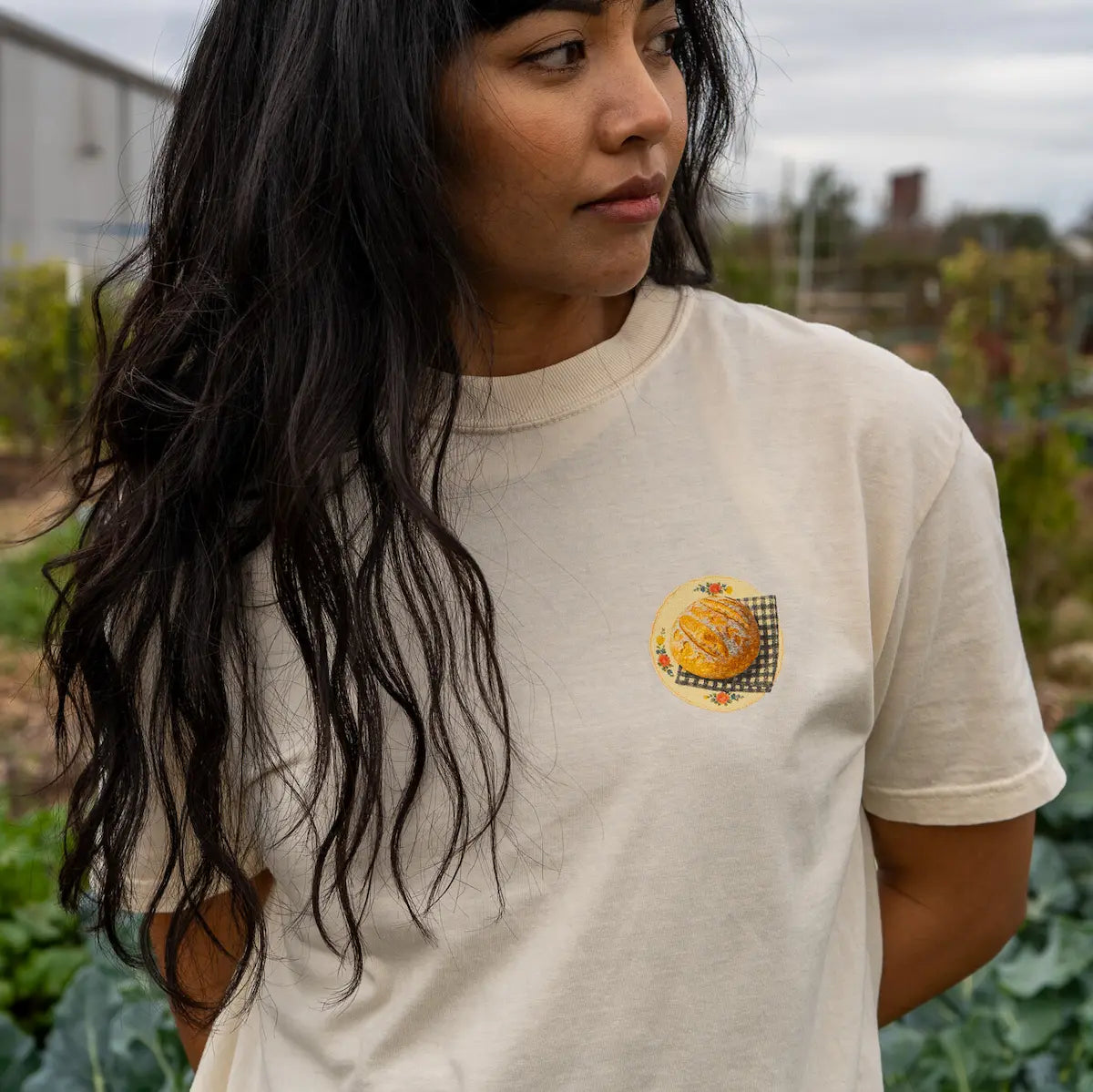 Person wearing a beige t-shirt with sourdough bread  in an outdoor setting