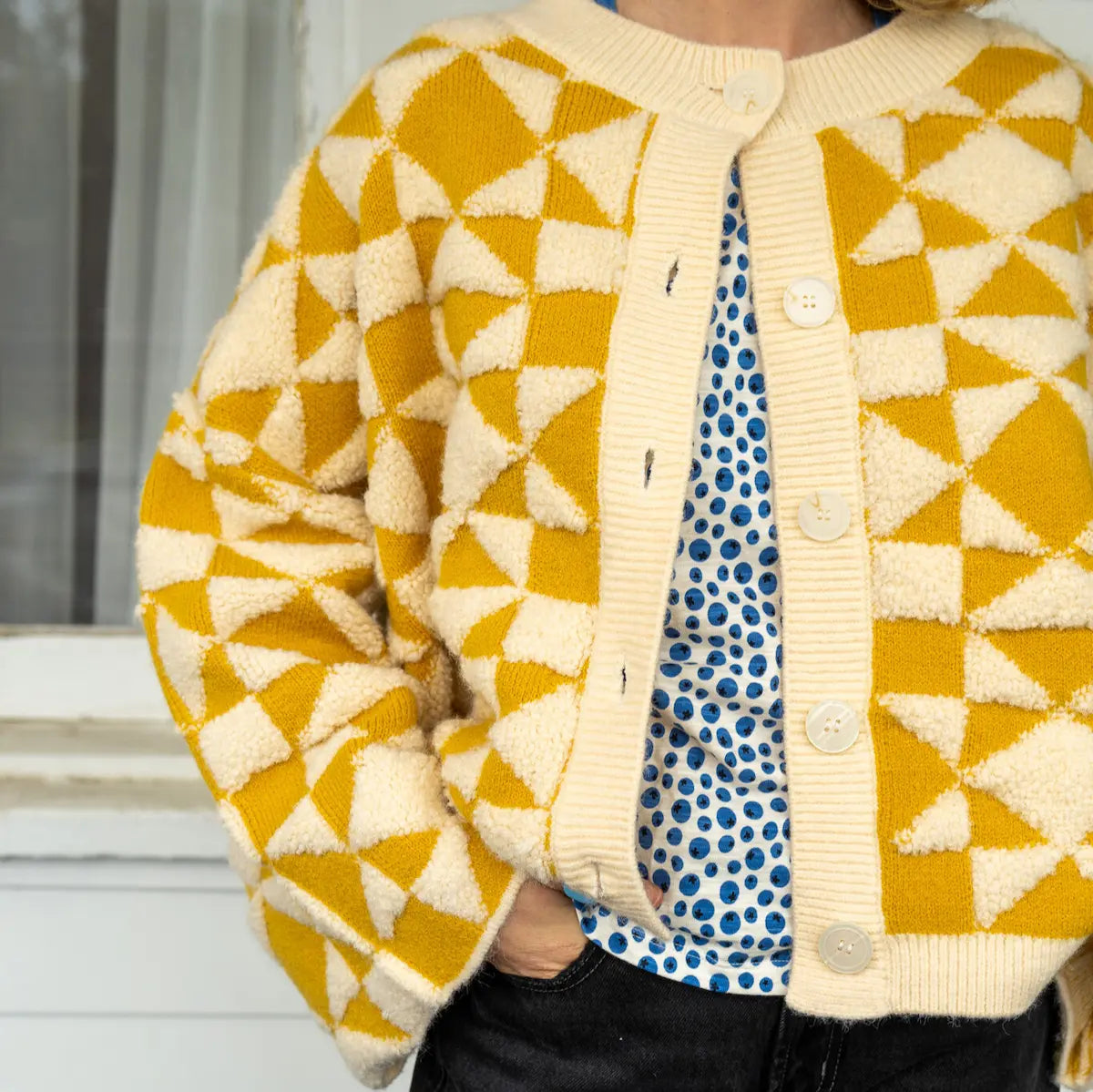 Person wearing a yellow and white geometric patterned cardigan outdoors.