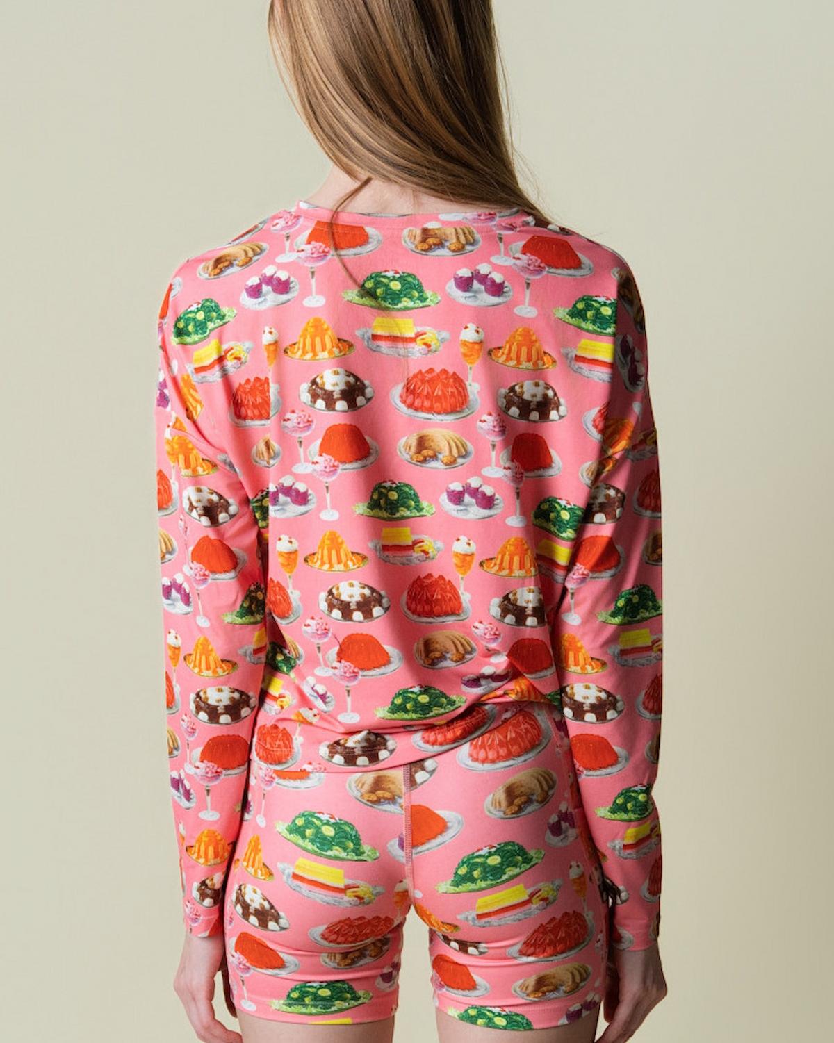 Person wearing a pink long-sleeve shirt and shorts with gelatin-themed pattern on a plain background