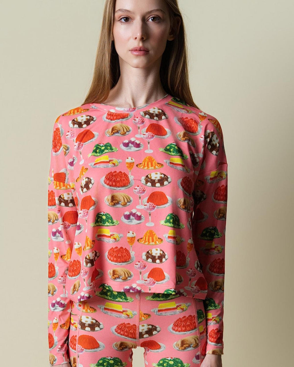 Model wearing a pink sweatshirt with colorful dessert pattern on a beige background