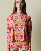 Model wearing a pink sweatshirt with colorful dessert pattern on a beige background