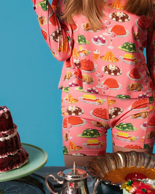 Person wearing a pink casual set with dessert print, standing next to a cake on a blue background.