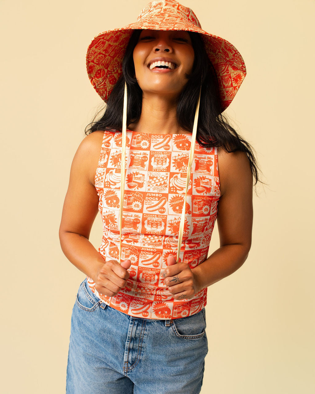 Person wearing a matching tank top and sun hat with orange vintage-style food coupon pattern and jeans.