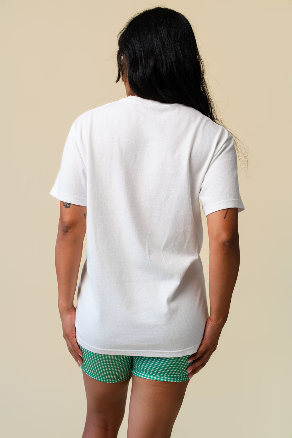 Back person wearing a white t-shirt on a beige background.