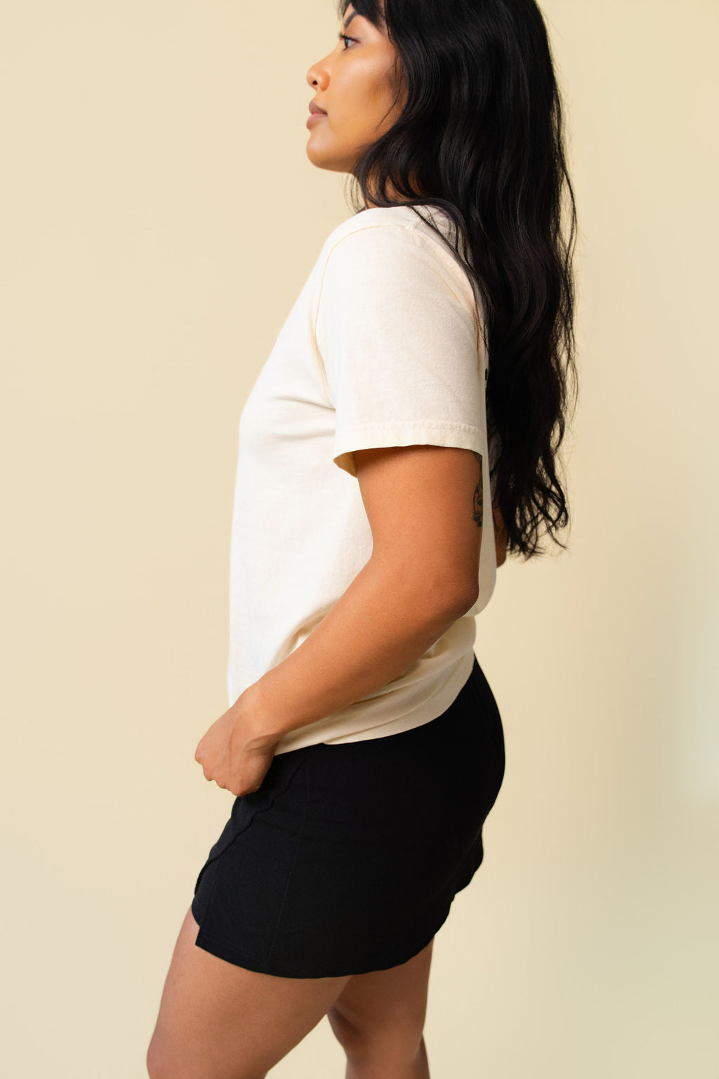 Side of person wearing a beige t-shirt on a beige background.