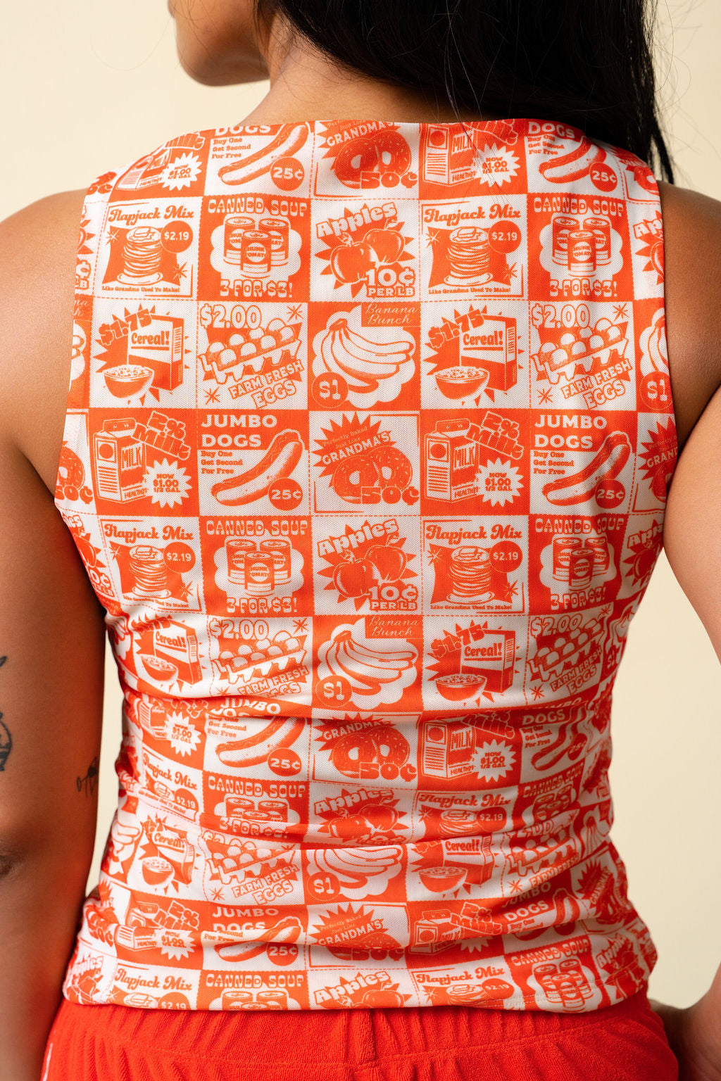 Back of person wearing a tank top with orange vintage-style food coupon pattern and jeans.