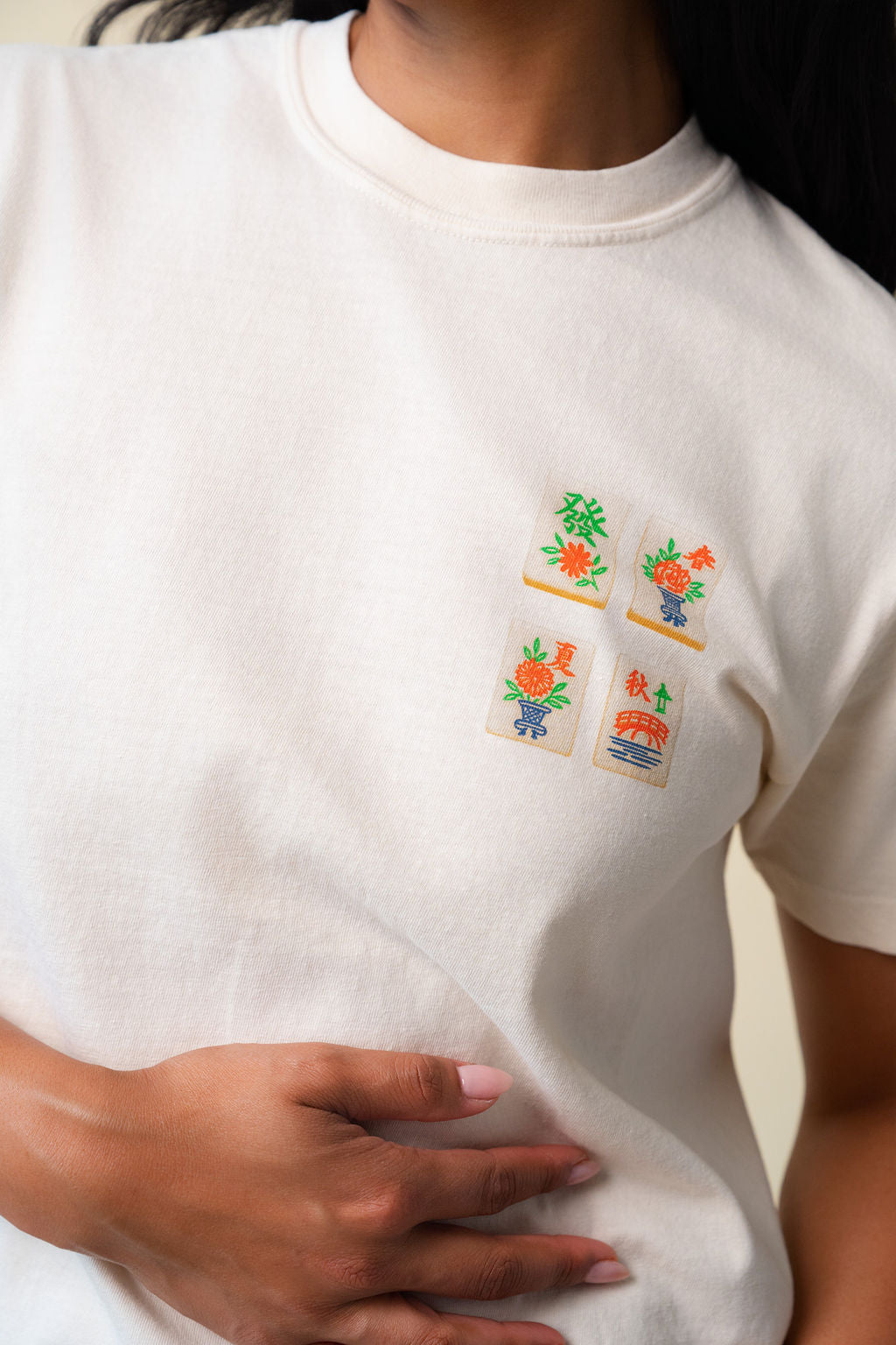 Close up of a person wearing a white t-shirt with a small design of mahjong. 