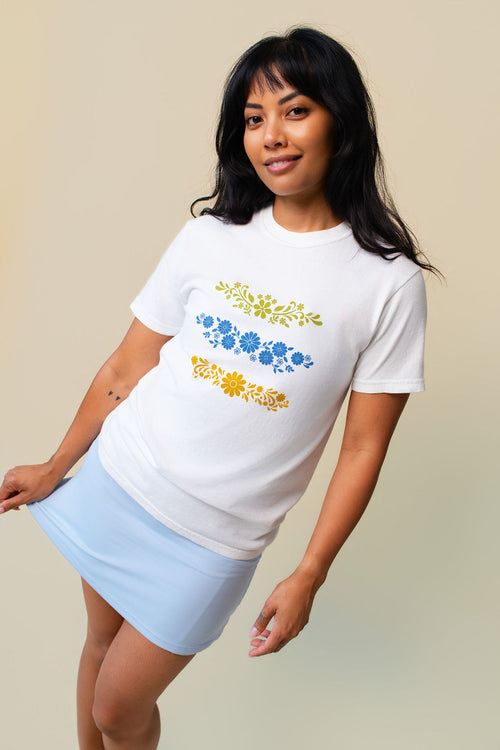 Person wearing a white t-shirt with floral designs on a beige background.