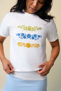 Person wearing a white t-shirt with floral designs on a beige background.