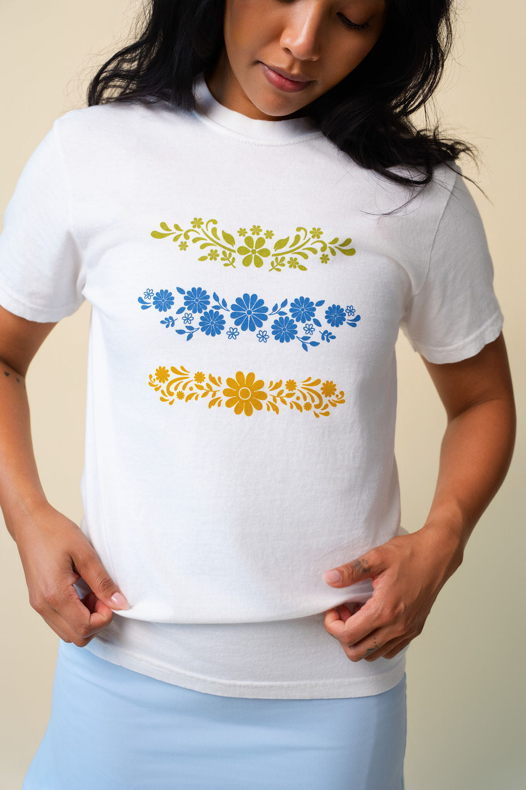 Person wearing a white t-shirt with floral designs on a beige background.