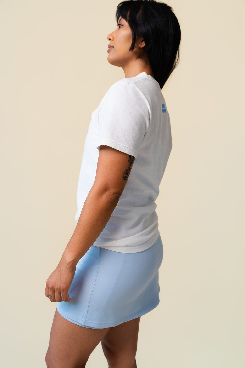Side of person wearing a white t-shirt with floral designs on a beige background.