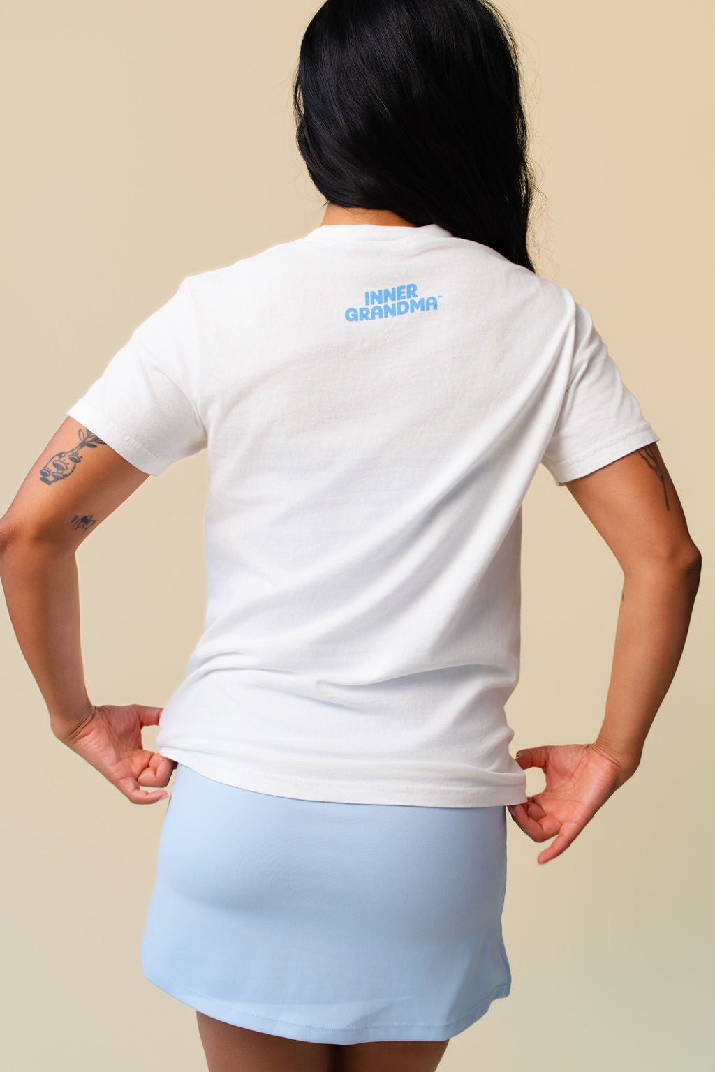Back of person wearing a white t-shirt with inner grandma printed in blue on a beige background.