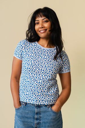 Person wearing a blueberry printed short sleeve paired with blue jeans standing on a beige background.