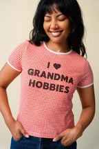 Person wearing a red and white checkered shirt with 'I ❤️ Grandma Hobbies' text and jeans on a beige background.