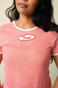 Person wearing a red and white gingham printed tee with a red and white "Tired" patch on the front. 