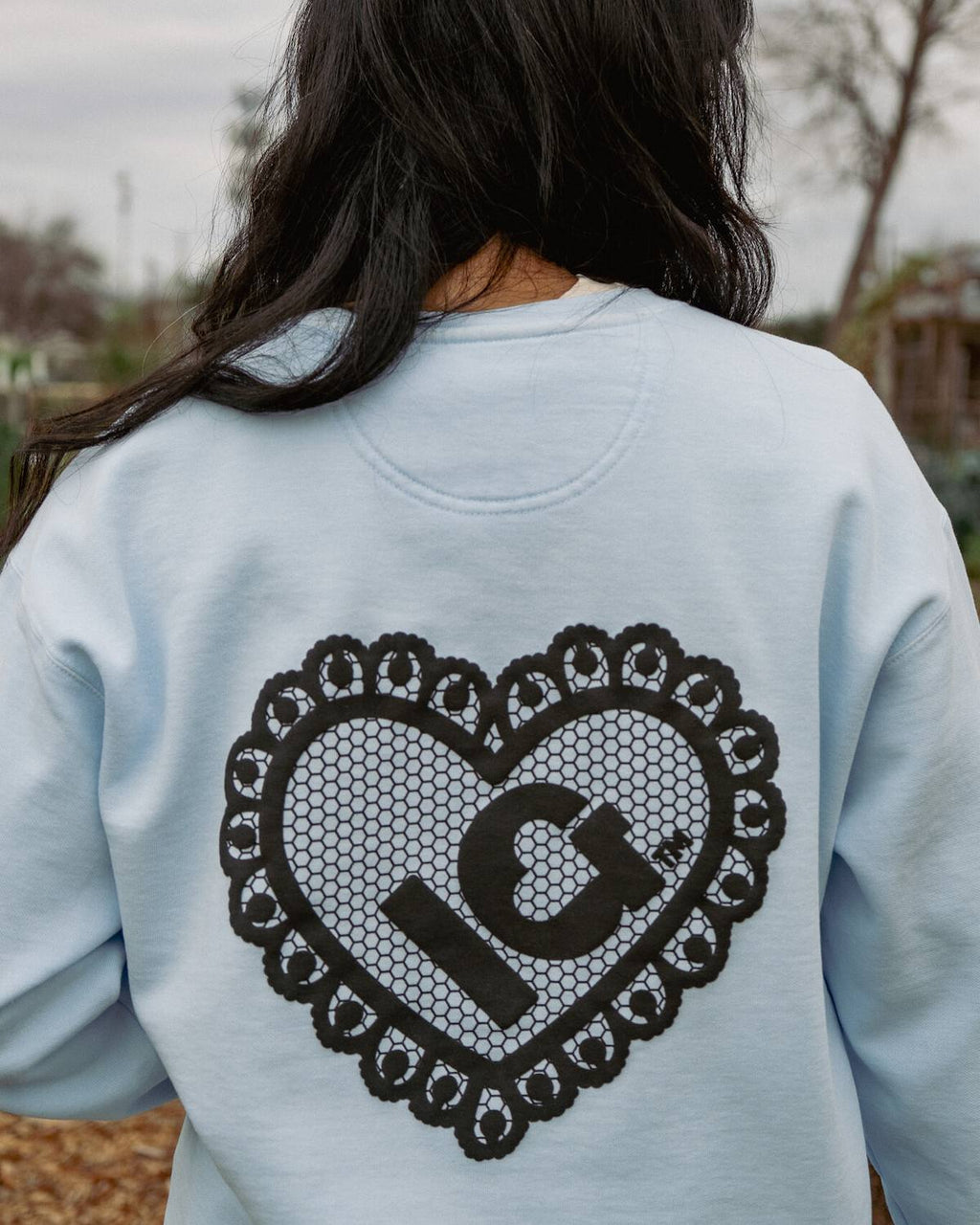 Light blue sweatshirt with black heart design and 'IG' logo on the back, worn by a person outdoors.