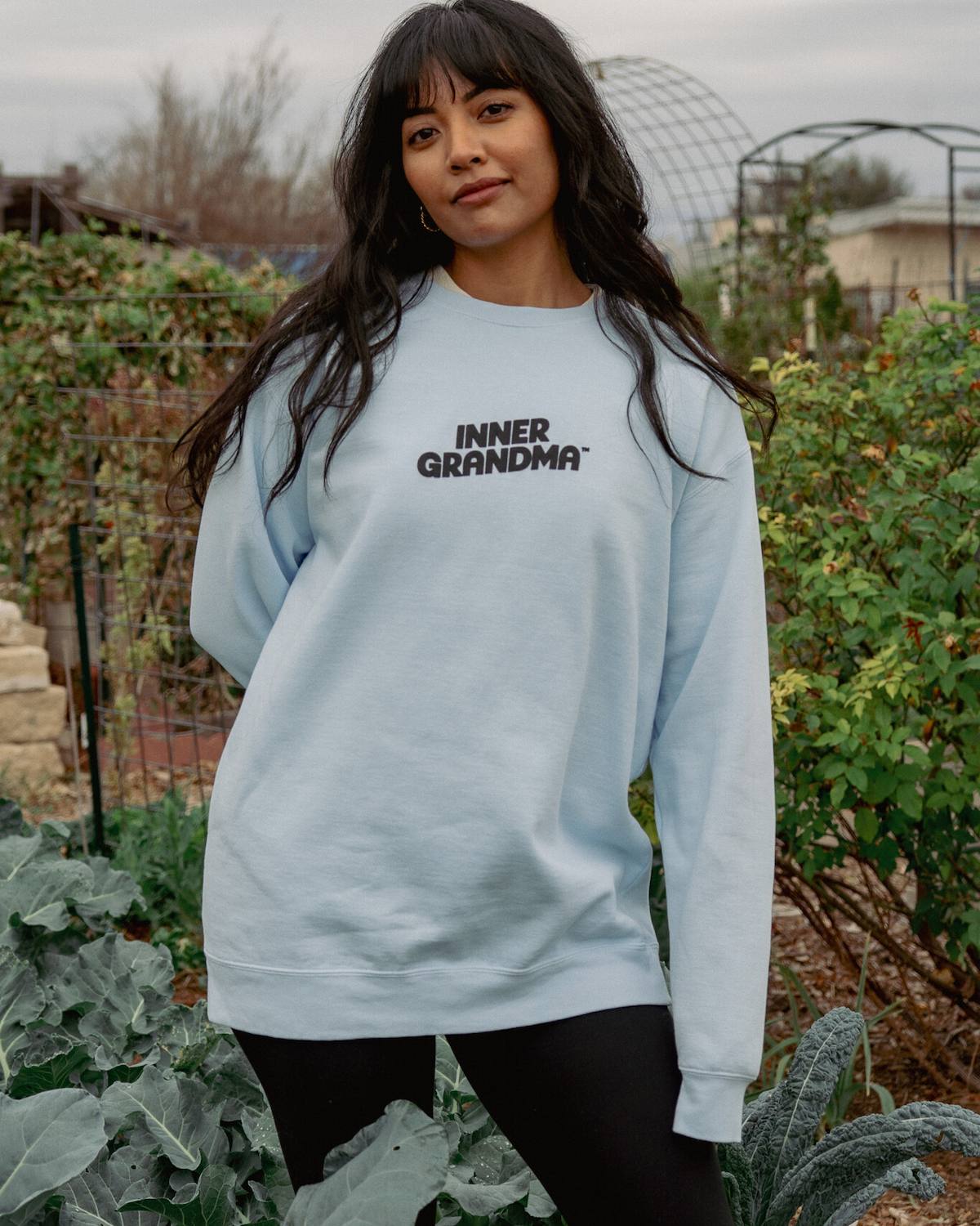 Woman wearing a light blue sweatshirt with 'INNER GRANDMA' text in an outdoor setting.