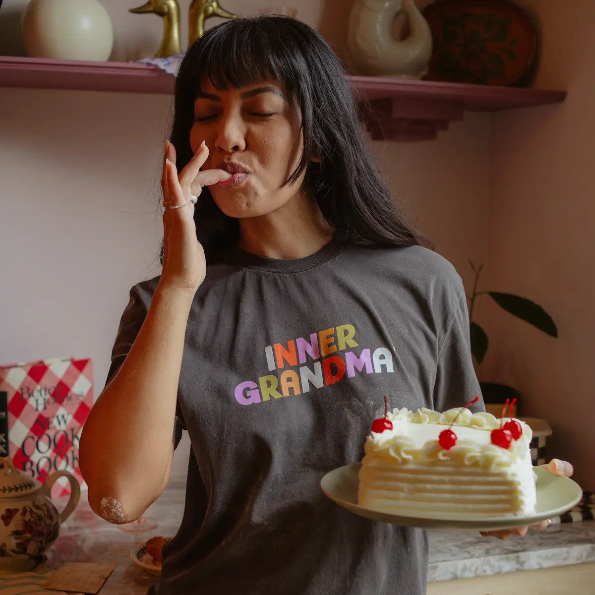 Woman wearing a 'Inner Grandma' shirt holding a cake in a kitchen setting