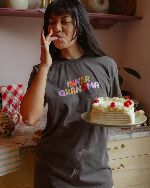 Woman wearing a 'Inner Grandma' shirt holding a cake in a kitchen.
