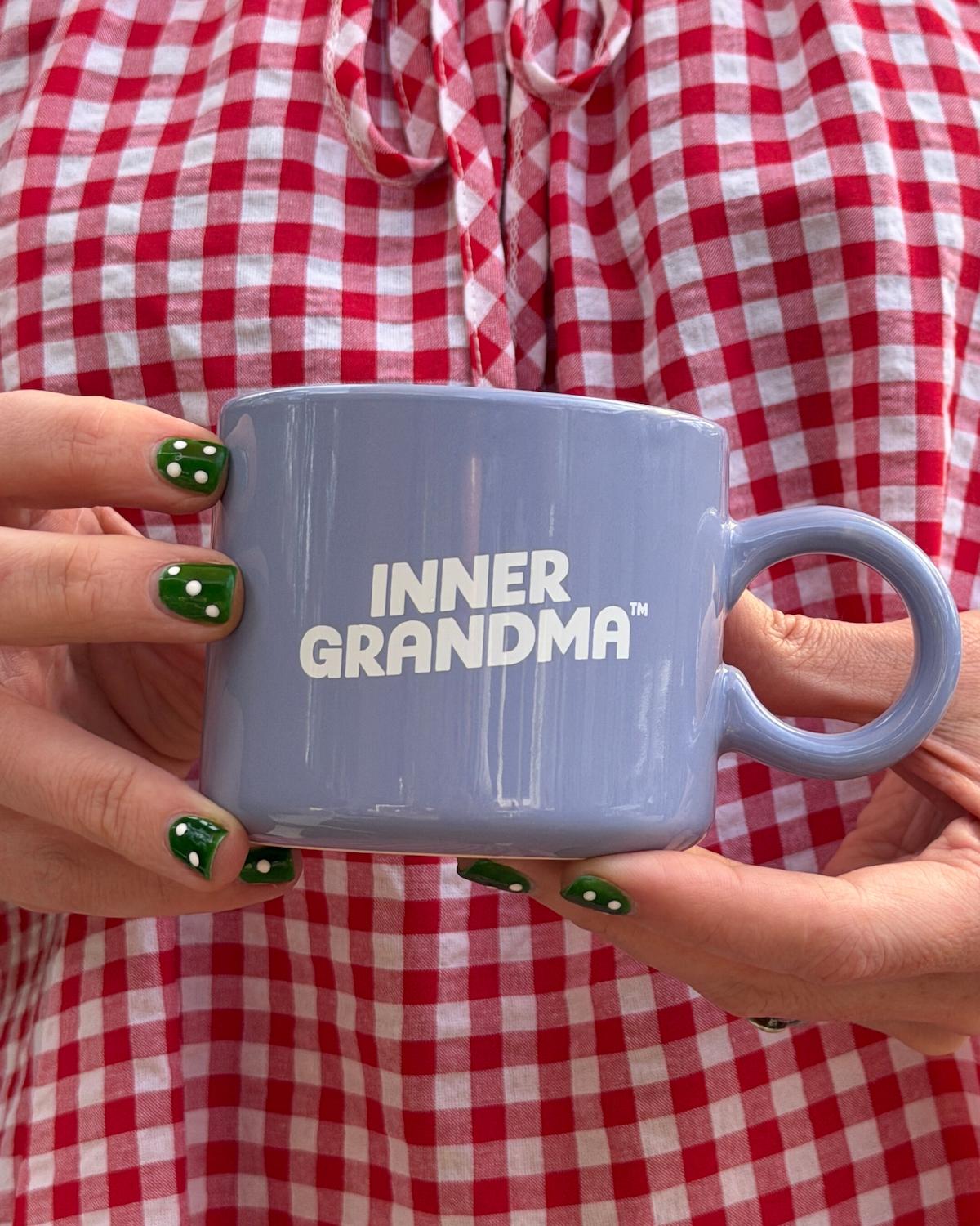 Person holding a blue mug with 'INNER GRANDMA' text against a red and white checkered background