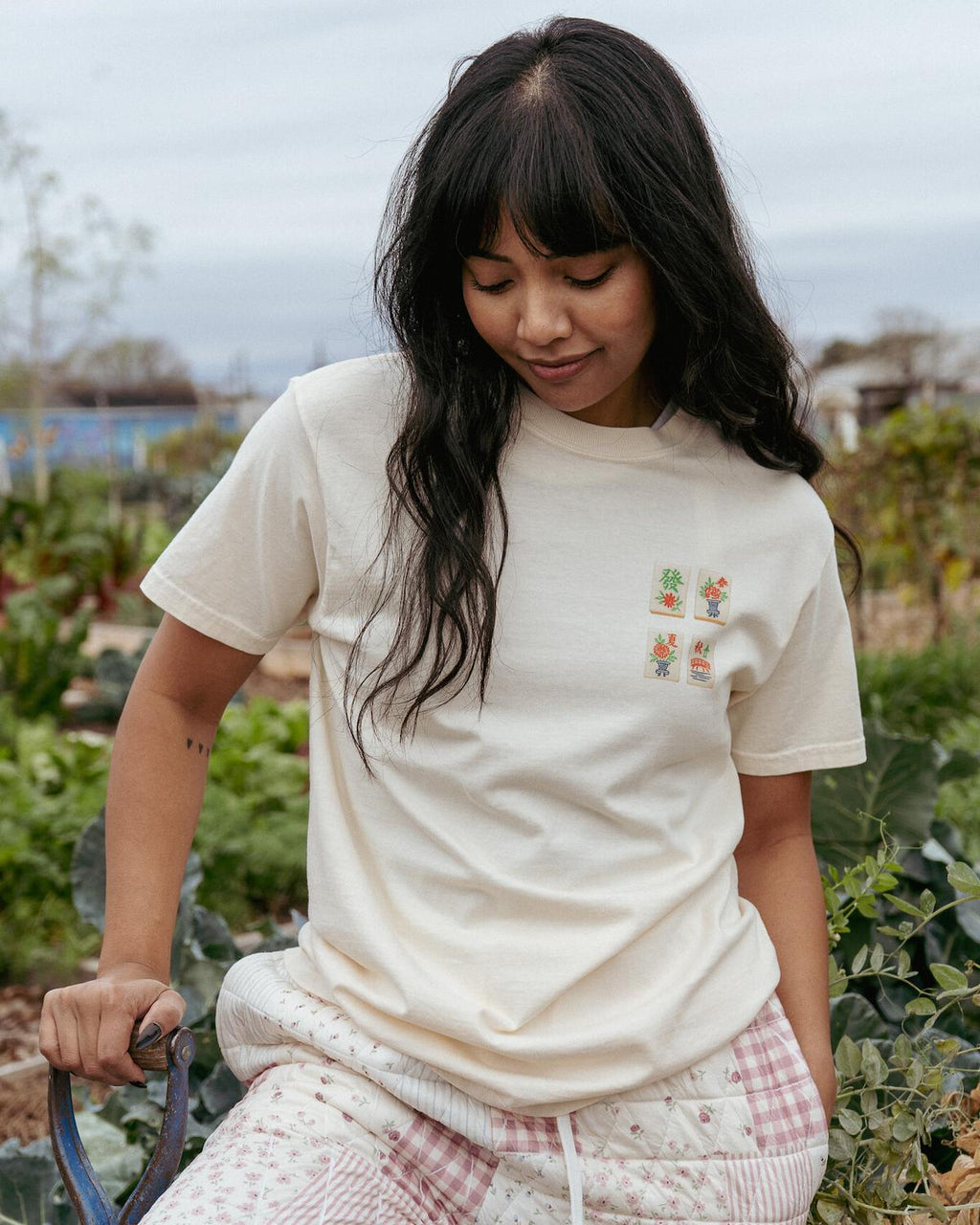 Woman wearing a white t-shirt with a small design, standing in an outdoor setting with greenery.