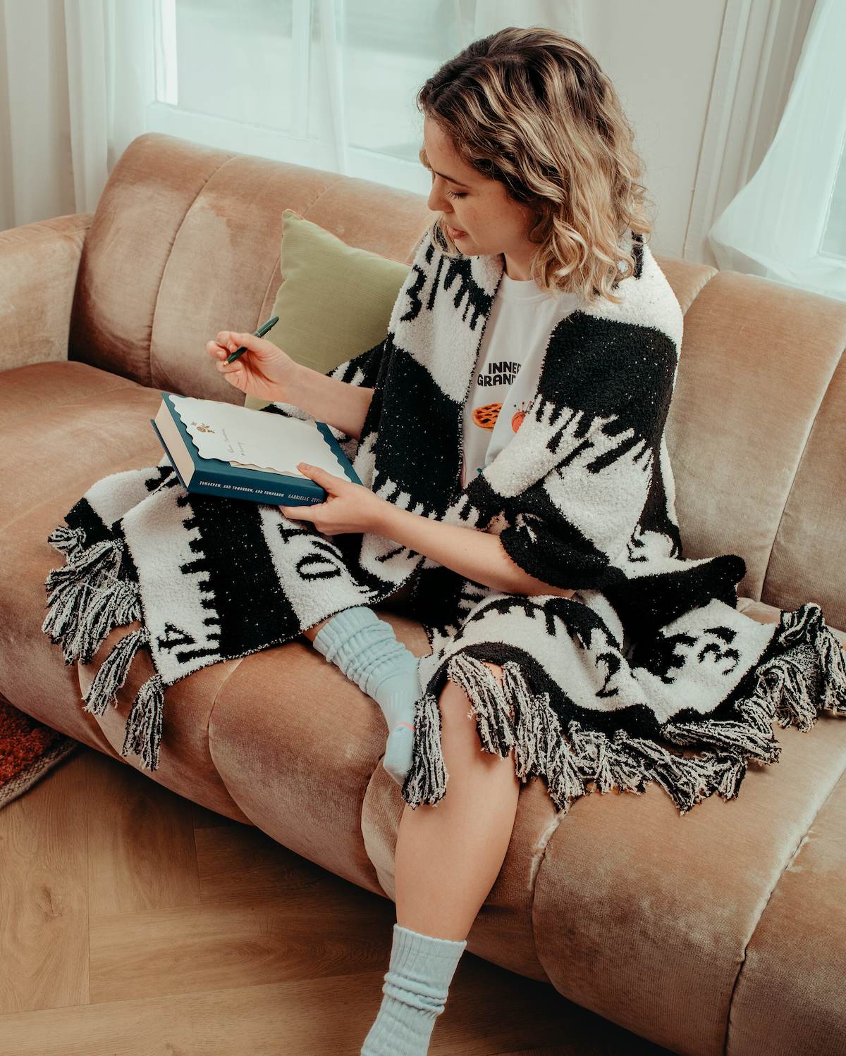 Woman sitting on a couch with a blanket, using a phone.