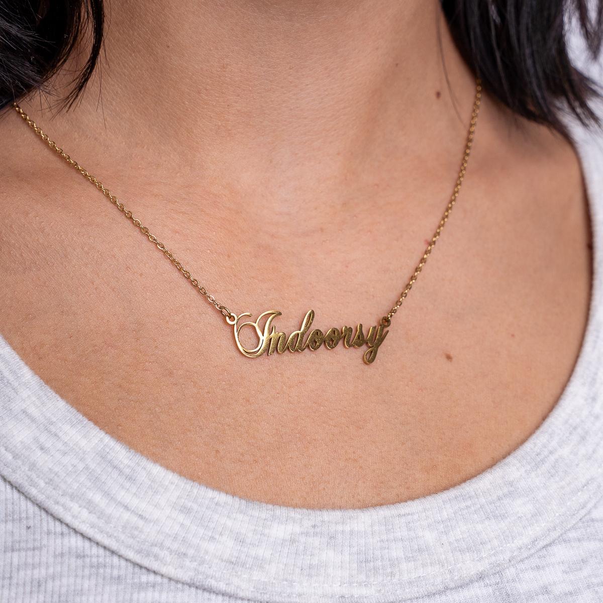Gold necklace with 'Indoor' pendant on a person wearing a white top.