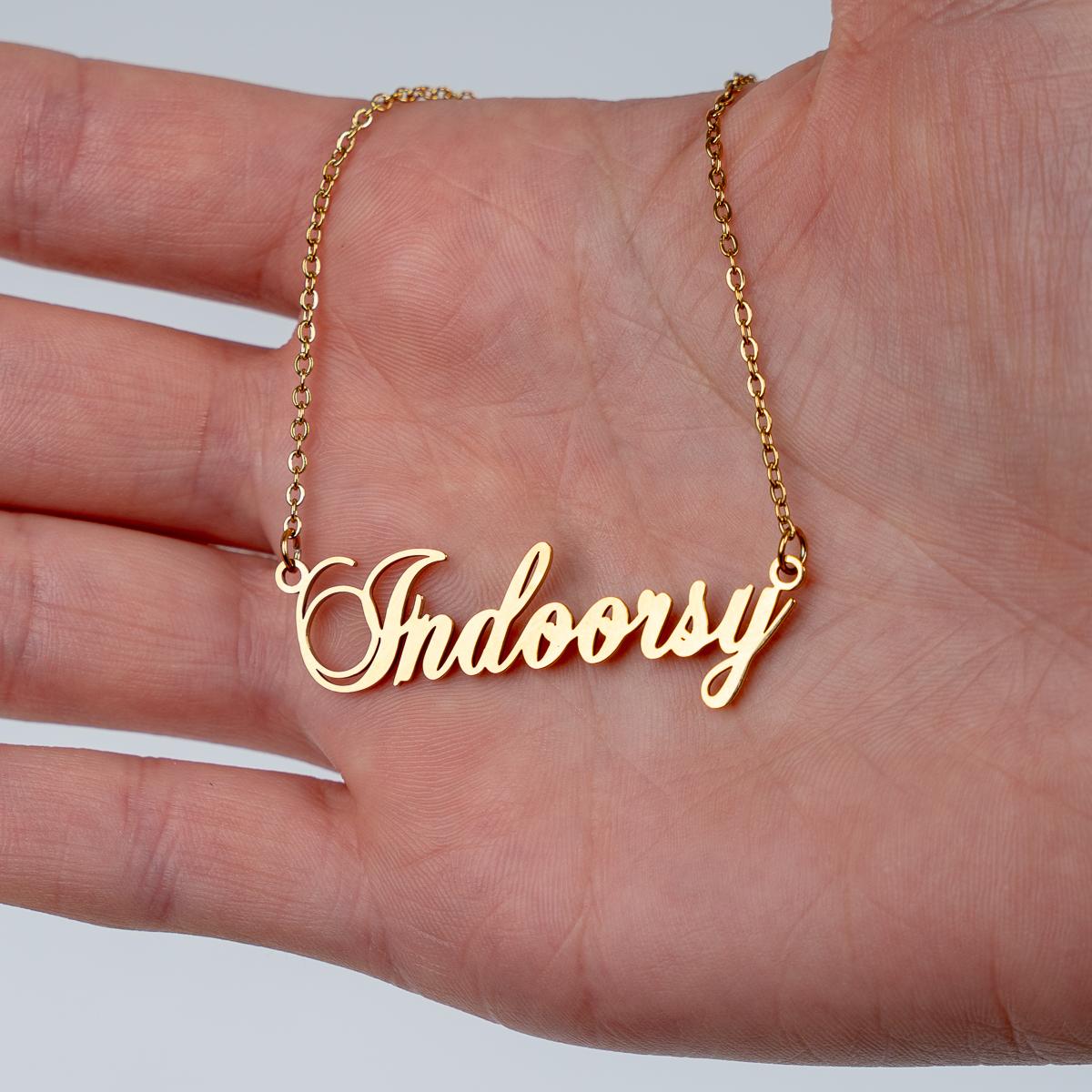 Gold necklace with 'Indoorsy' pendant held in a hand against a light background