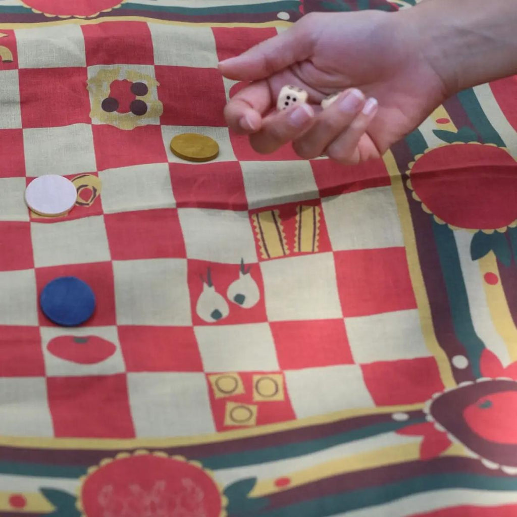 Hand holding small dice over a colorful checkered fabric with cartoon designs