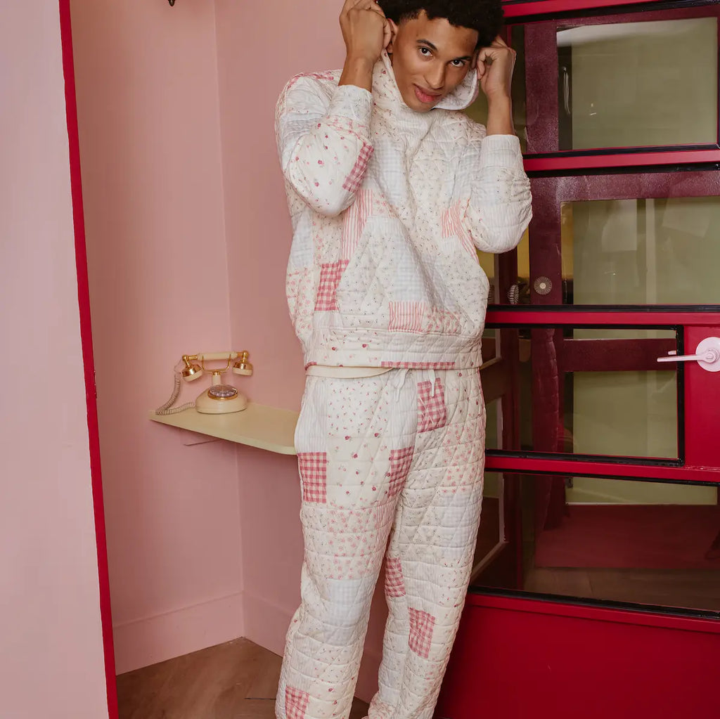 Person wearing a matching patchwork designed outfit in a room with pink walls and a red wardrobe.