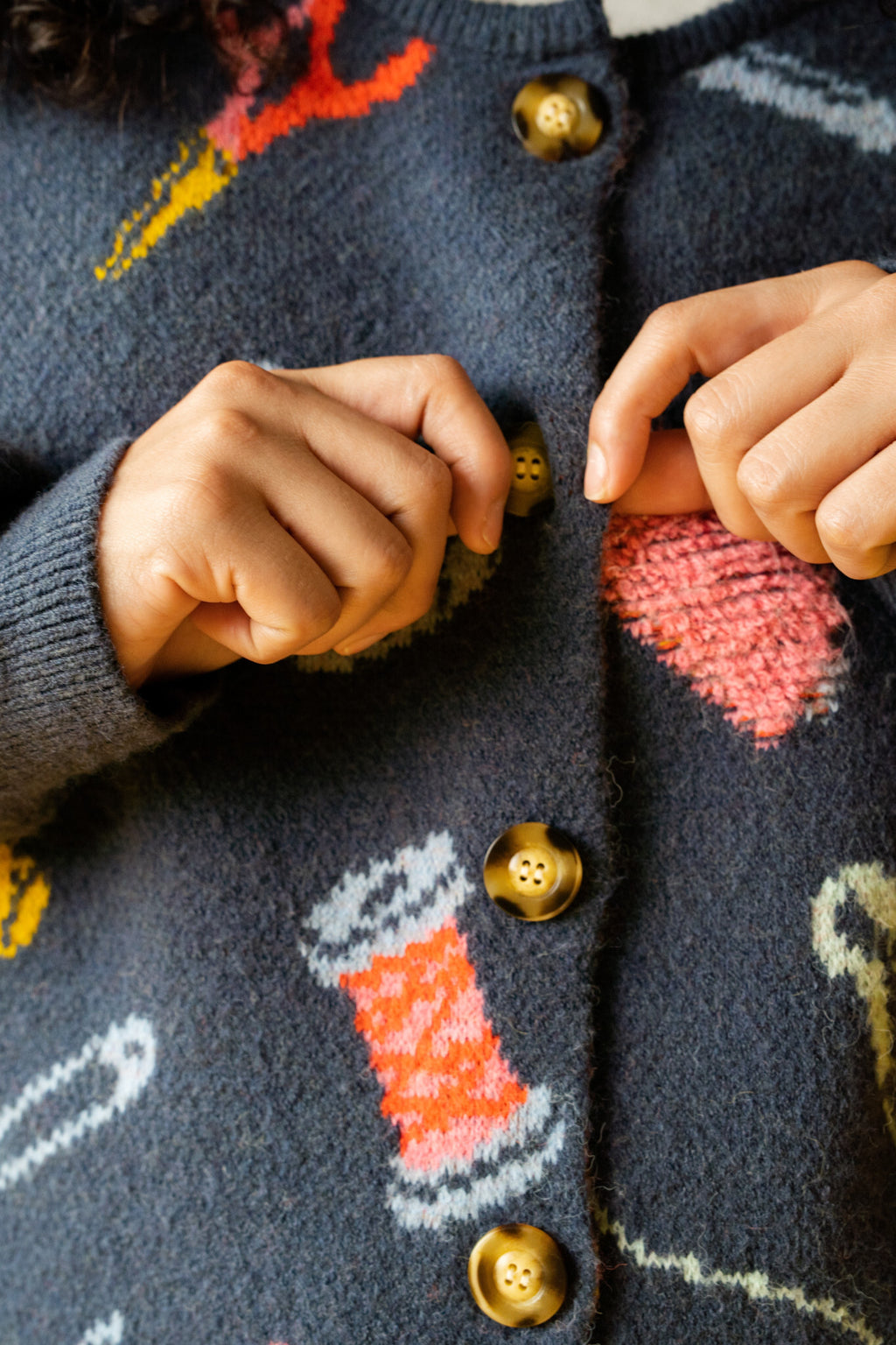 Close-up of a person wearing a dark blue knitted sweater with colorful sewing item pattern and buttons.