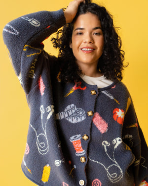 Person wearing a colorful sweater with sewing items on it and jeans on a yellow background. 