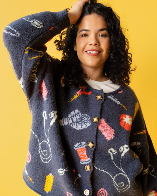 Person wearing a colorful sweater with sewing items on it and jeans on a yellow background. 
