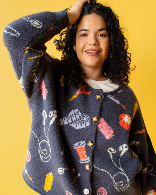 Person wearing a colorful sweater with sewing items on it and jeans on a yellow background. 