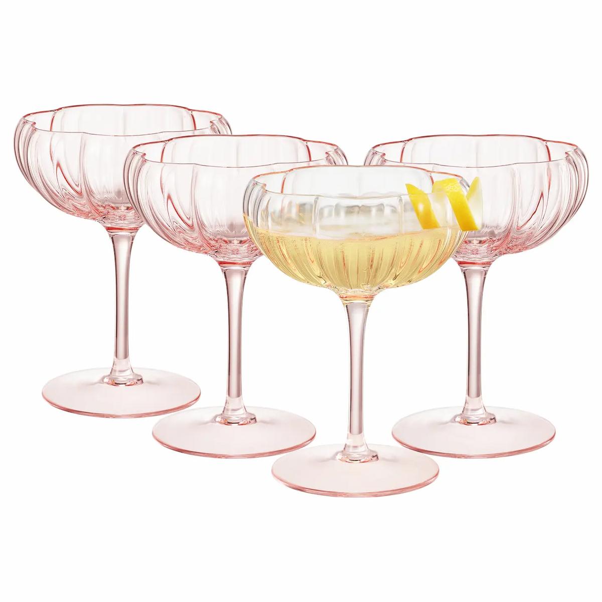 Set of four pink cocktail glasses with a drink and lemon garnish on a white background