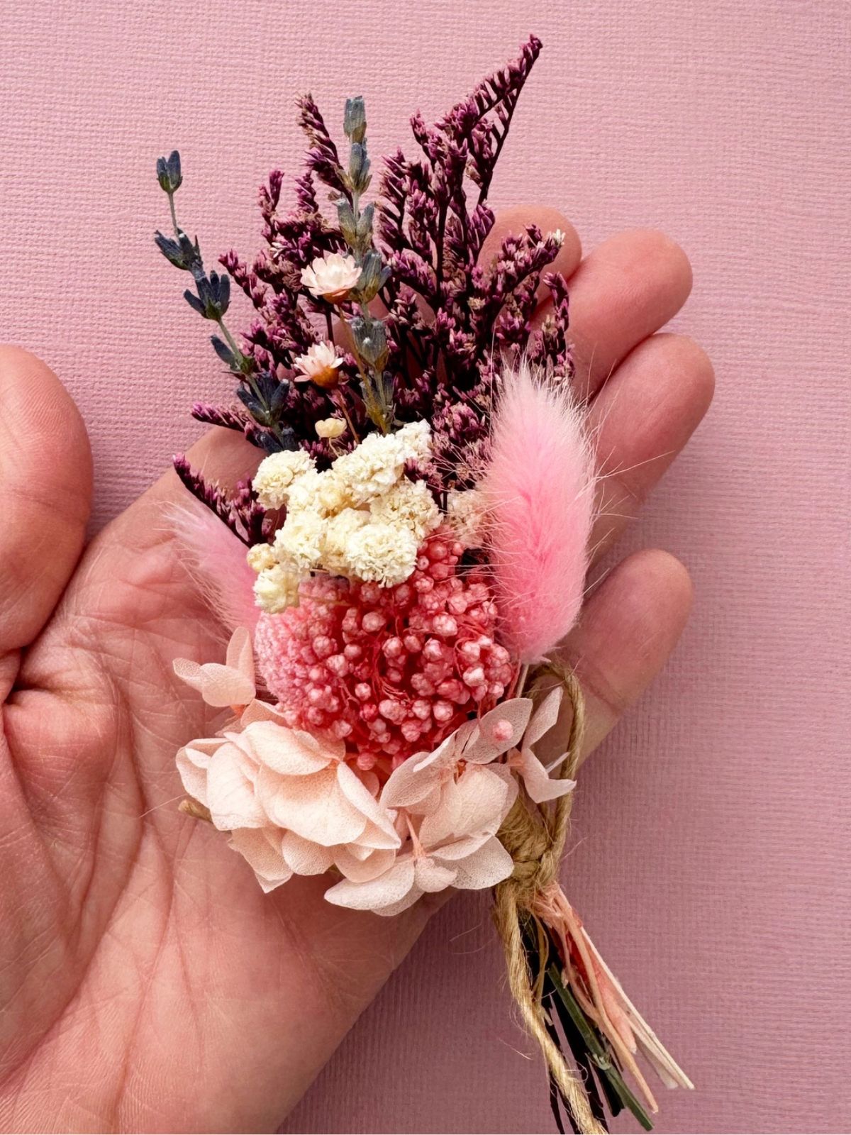 Small bouquet of flowers held in a hand against a pink background