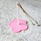 Pink flower-shaped holder with a white yarn spinner and gold-wrapped white object on a textured gray surface
