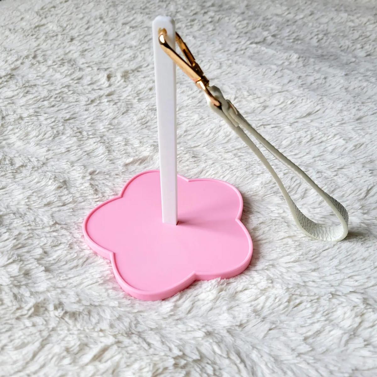 Pink flower-shaped holder with a white yarn spinner and gold-wrapped white object on a textured gray surface