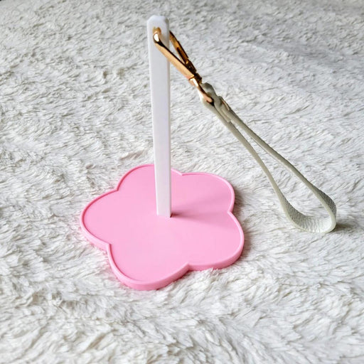 Pink flower-shaped holder with a white spinner and gold-wrapped white object on a textured gray surface
