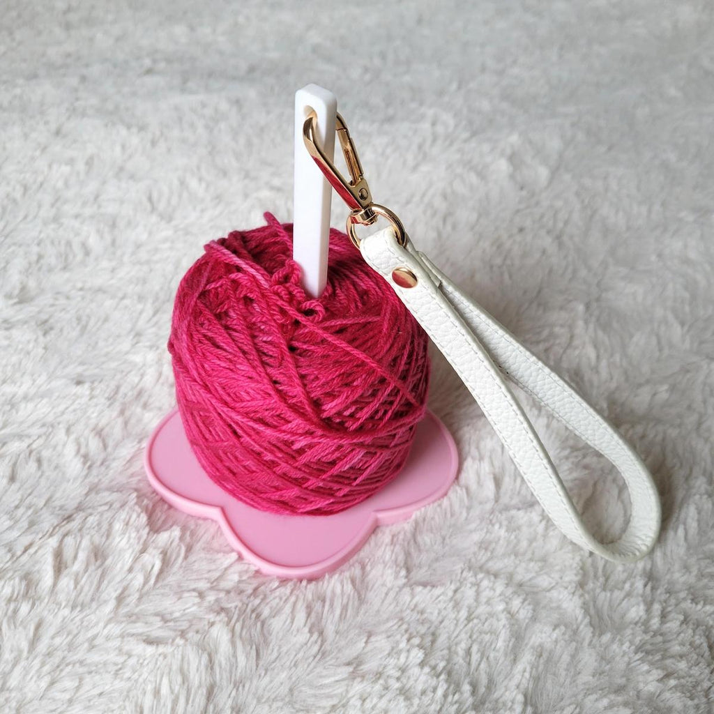 Pink yarn ball on a pink holder with a white strap on a white background