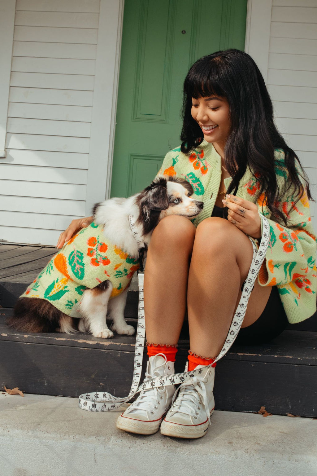 Woman in a veggie print sweater sitting on a step with a dog, both wearing matching outfits.