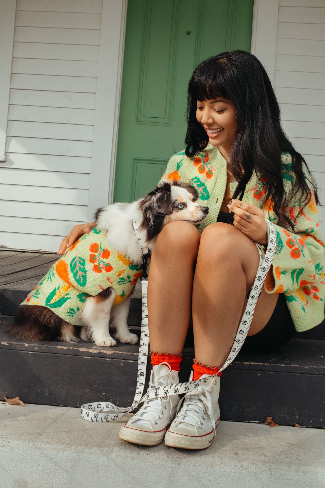 Woman in a veggie print sweater sitting on a step with a dog, both wearing matching outfits.